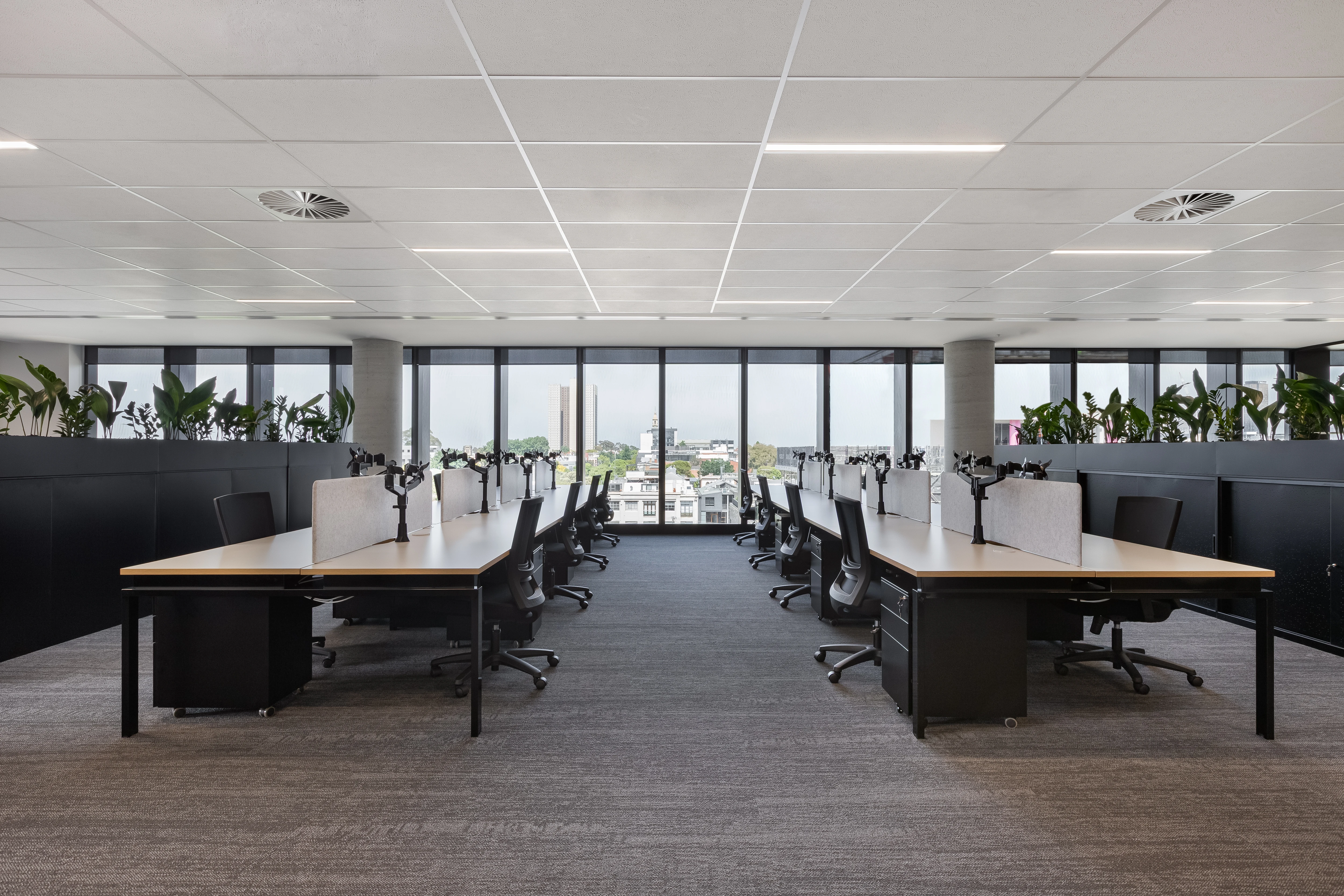Benchwork workstation with Logic monitor arms, an Arc acoustic screen and a Sonic task chair beside planter display shelving