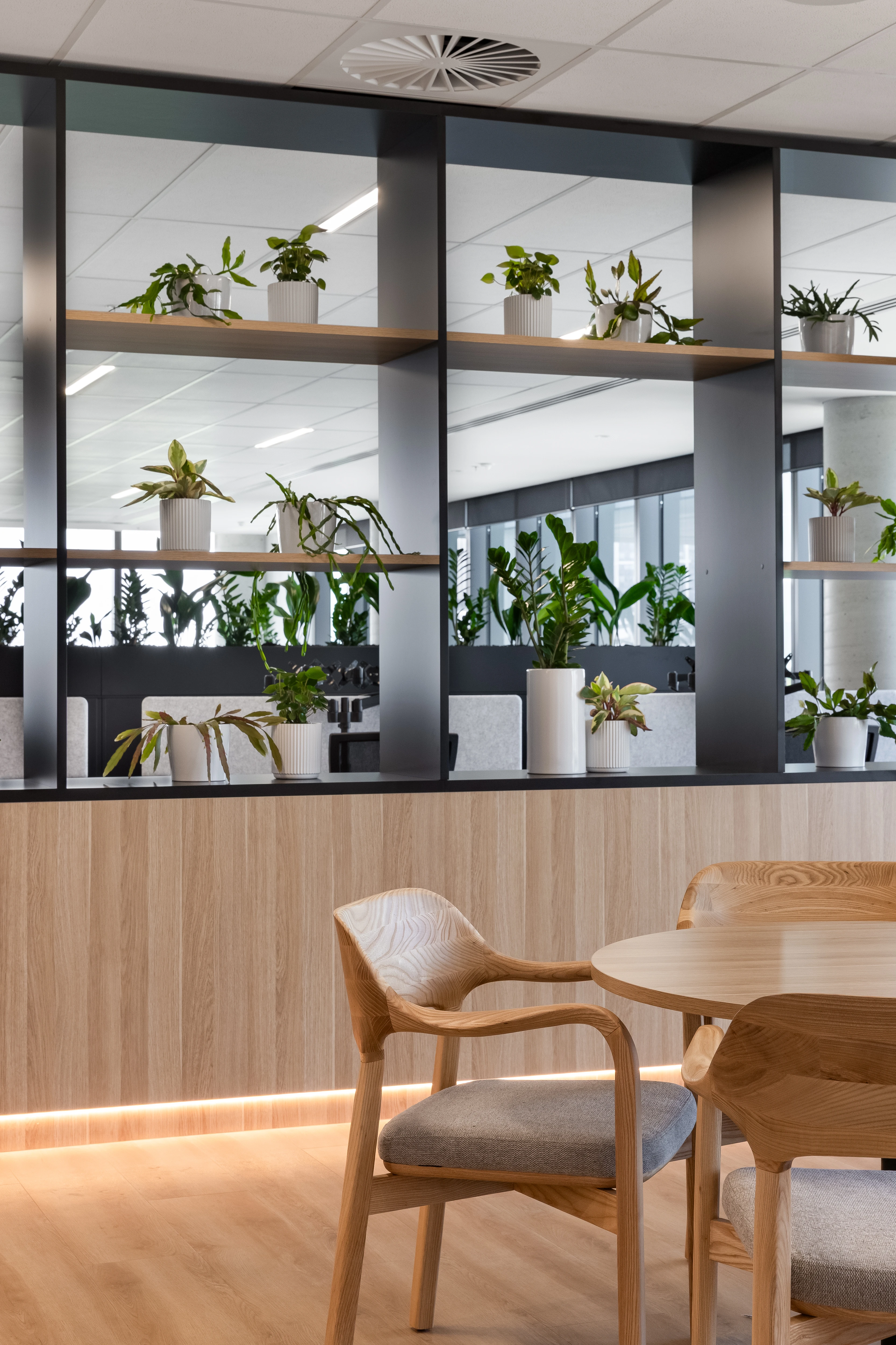 Taro timber chairs with soft grey upholstered pads at a circular Cosmopolitan table beside the curved glass facade