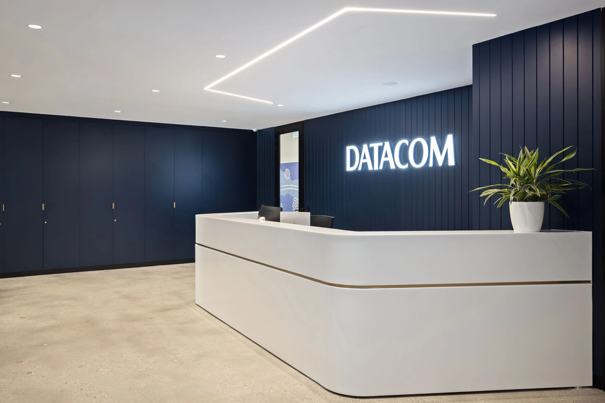 Datacom reception with deep midnight blue joinery wall panelling, illuminated signage and a curved white reception counter