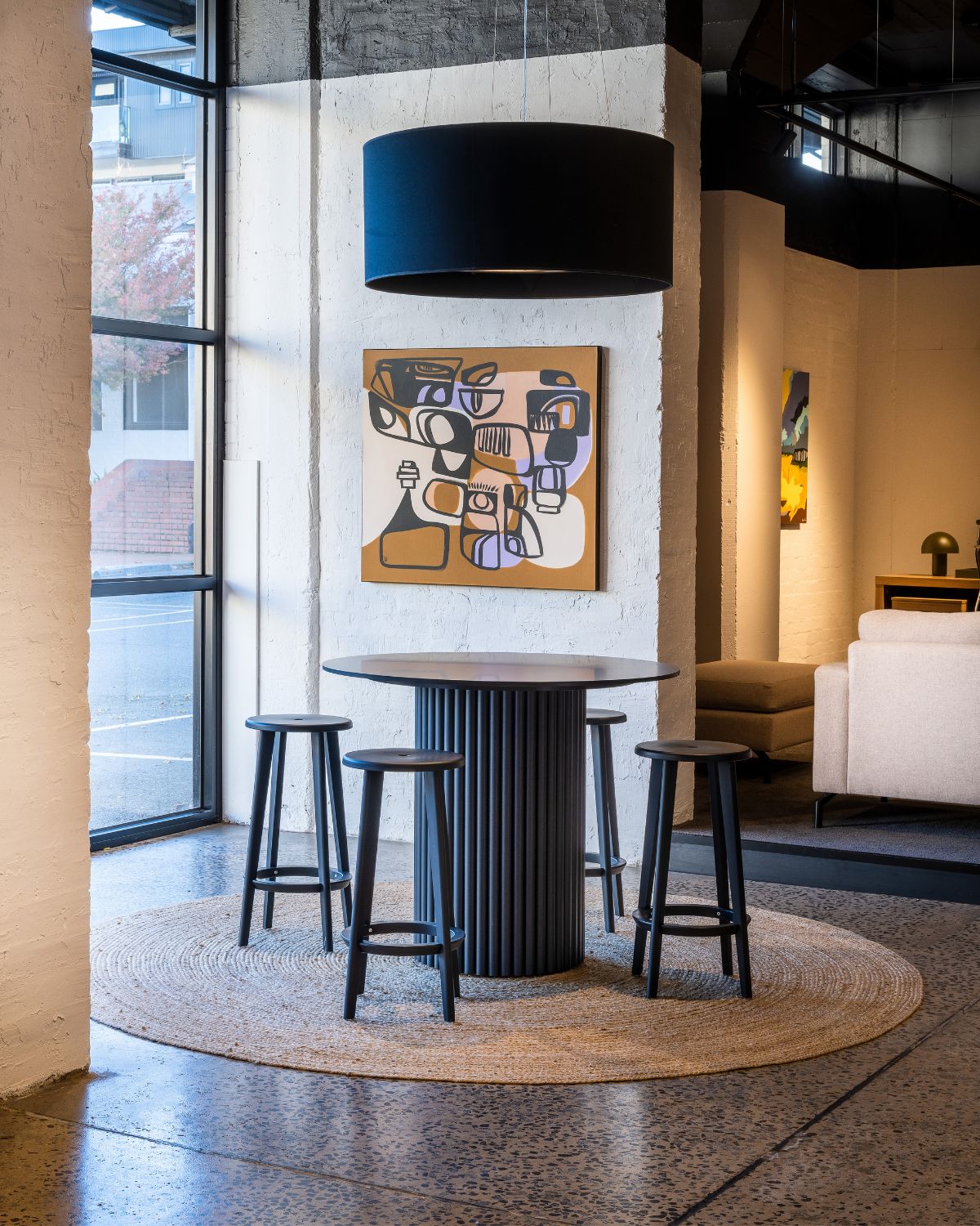Black round bar table and stools beneath a drum pendant in a Krost showroom