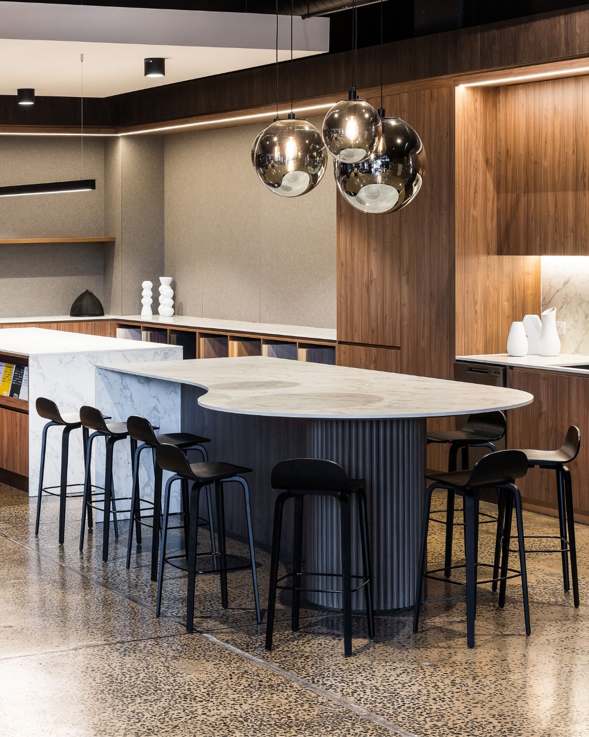 Curved marble-look island bench with black stools and smoked glass pendants