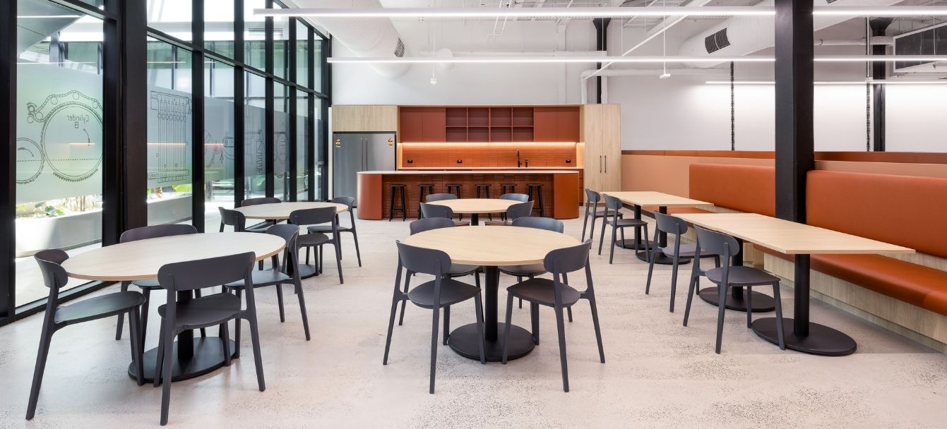 Breakout zone with round café tables, chairs and orange banquette seating beside tall windows