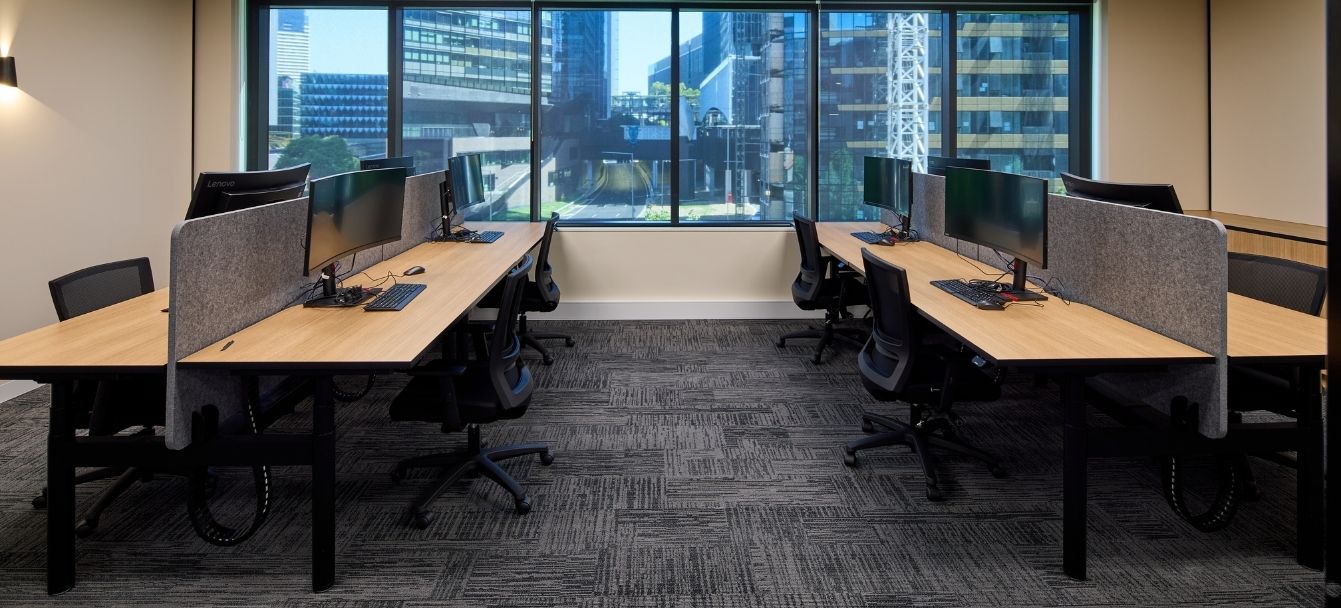 Open-plan height-adjustable workstations with Daily screens and black task chairs in front of city-view windows