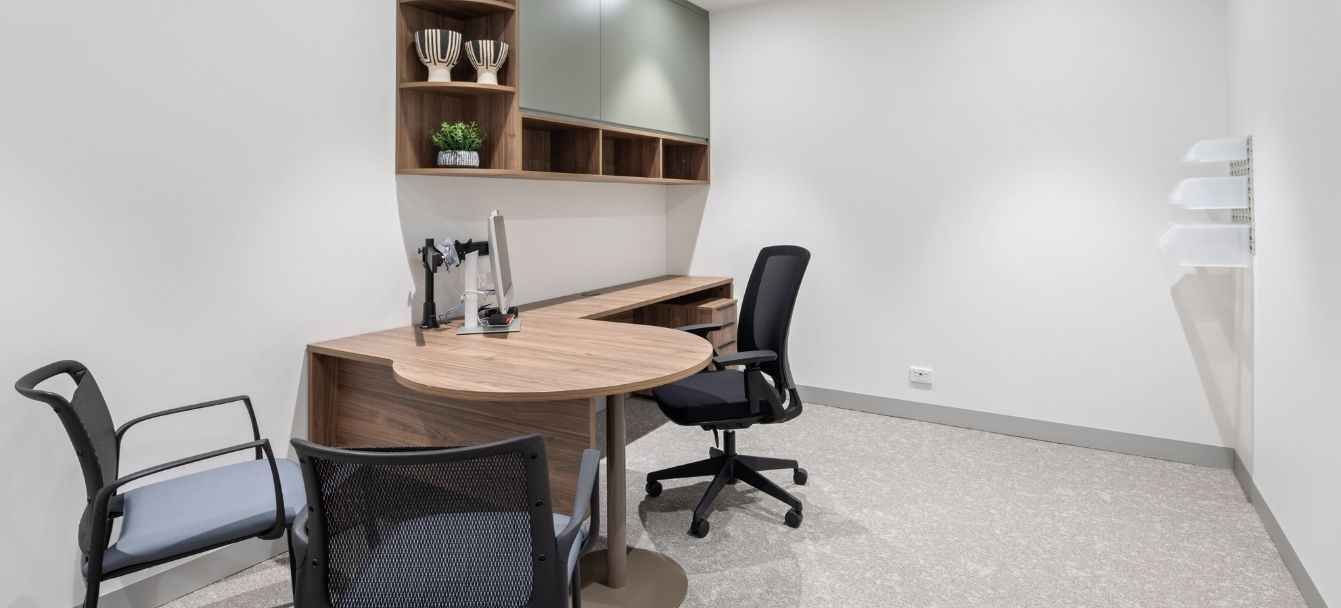 Consulting room with an oak desk, integrated shelving and black chairs
