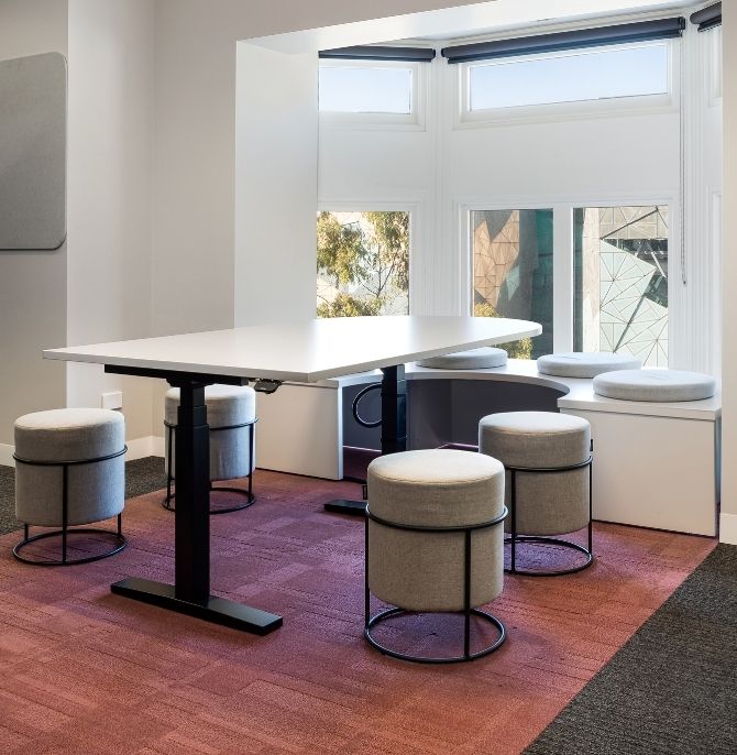 Height-adjustable Swish desk with Stax stools on a red rug beside the windows