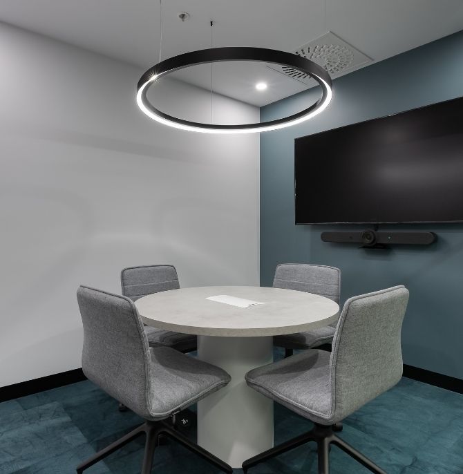 Meeting room with a round table, grey upholstered Alex chairs and a circular pendant light
