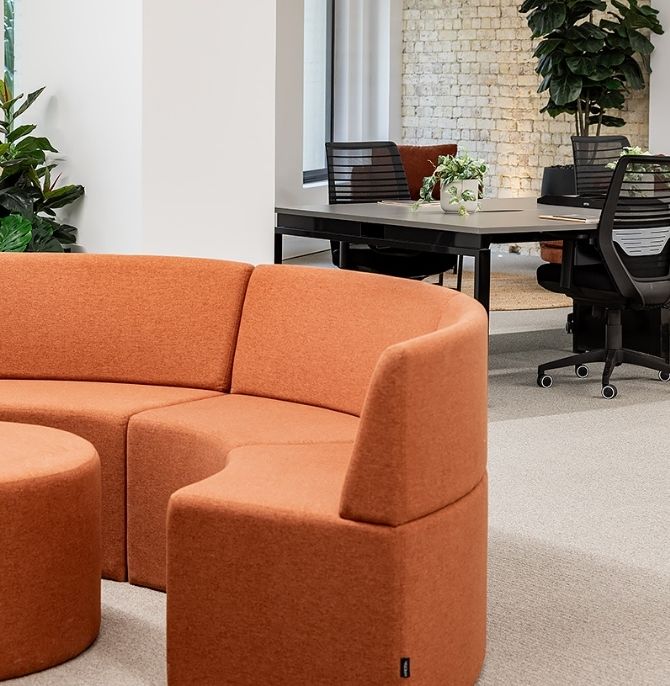 Orange curved Sofi ottomans upholstered in custom fabric in the breakout area