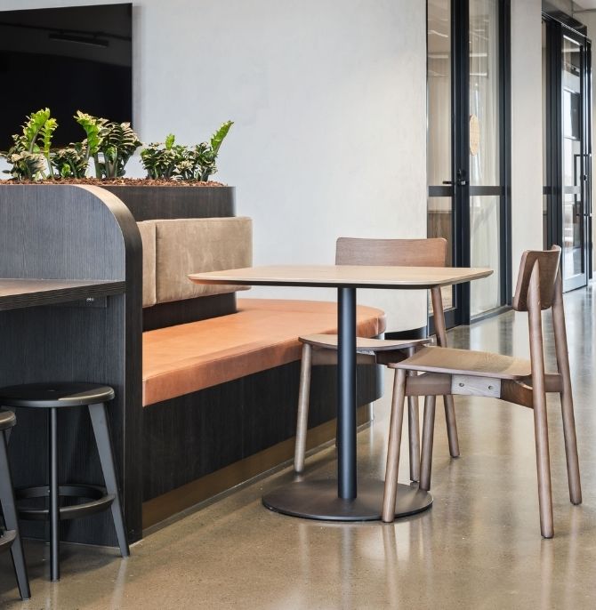 Booth seating in orange upholstery with a round table and timber chairs beneath a planter